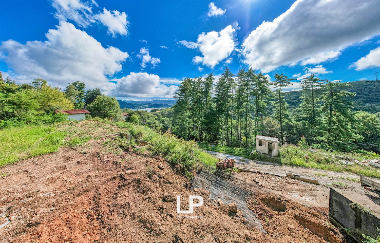 Excavations site, sloped land, grassy areas, trees, distant mountain views, lake in the distance, pathway, utility pole