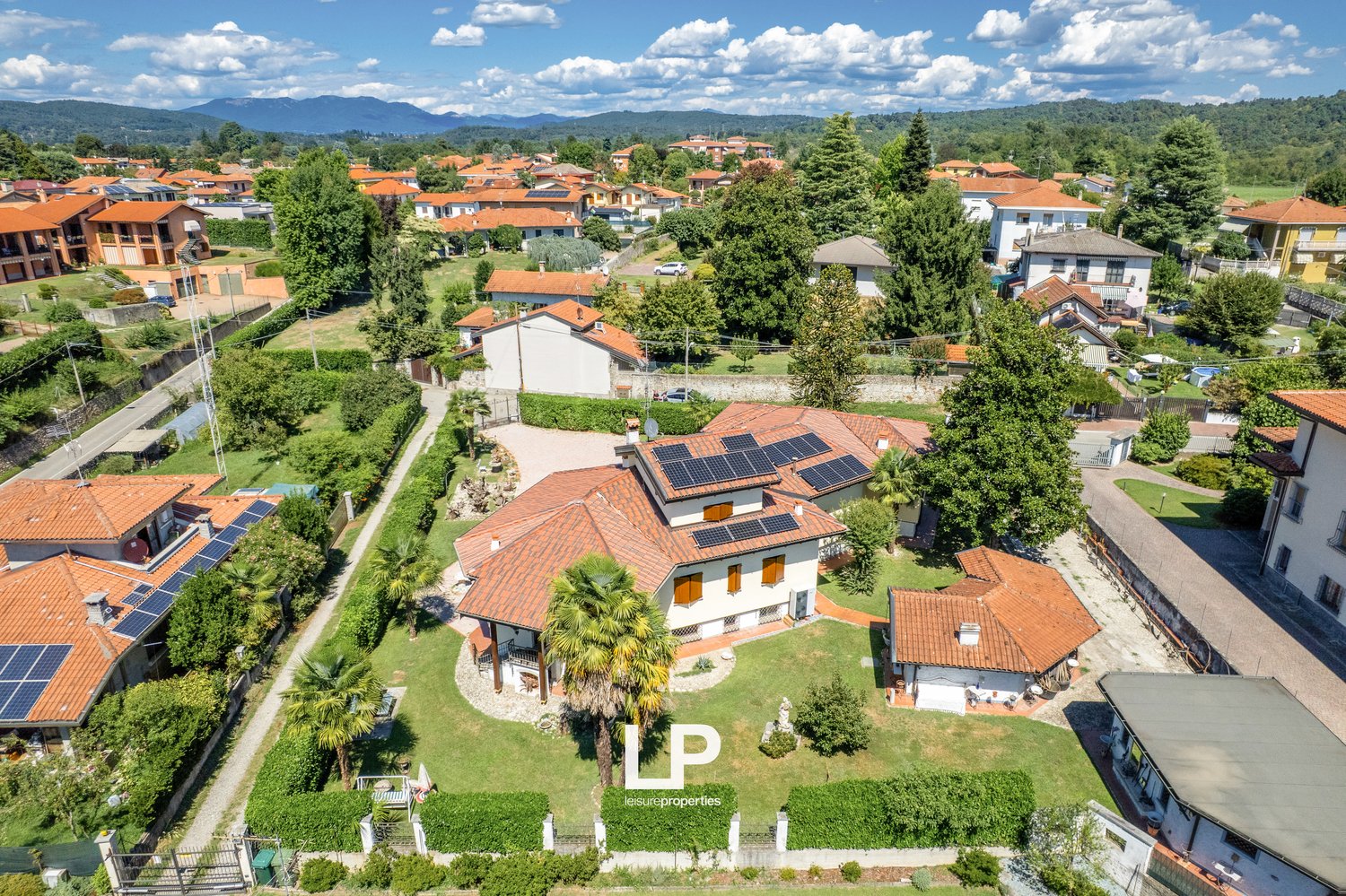Multiple houses, solar panels on roofs, driveway, garden, greenery, trees, distant mountains, aerial view