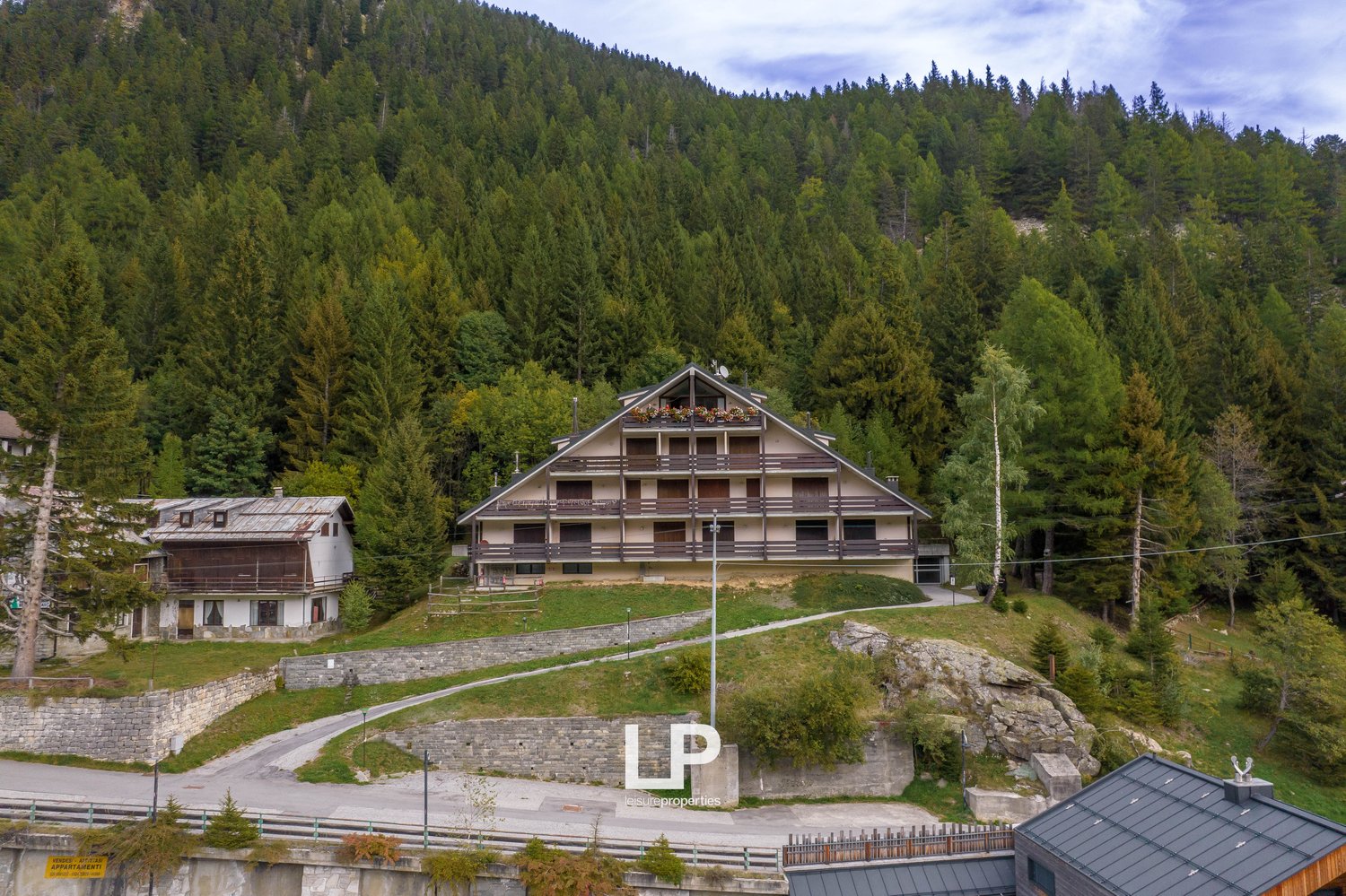 Large apartment building, nestled in a mountainous setting, surrounded by trees, with a scenic mountain backdrop