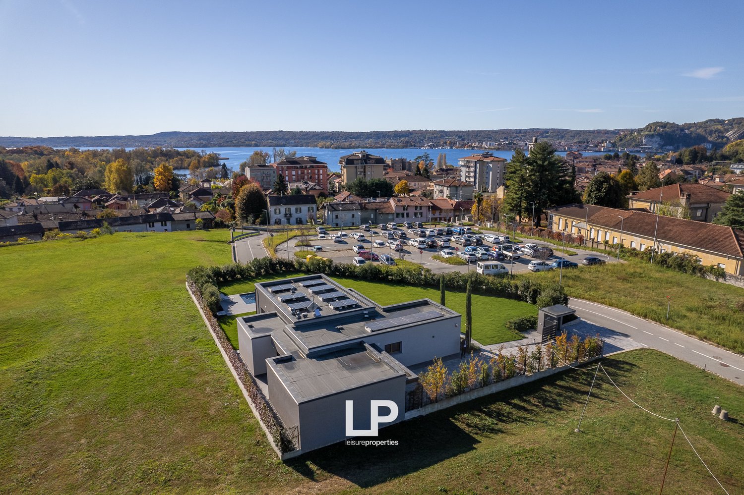 Modern building, solar panels on the roof, landscaped surroundings, parking lot, lush green fields