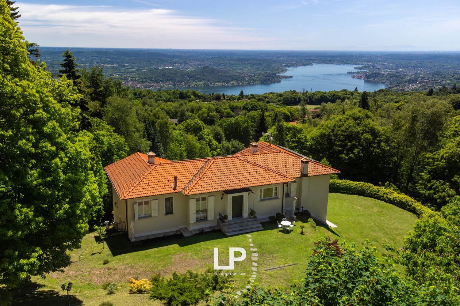 House with terracotta roof, set on a hillside, surrounded by greenery, overlooking a valley and a lake.