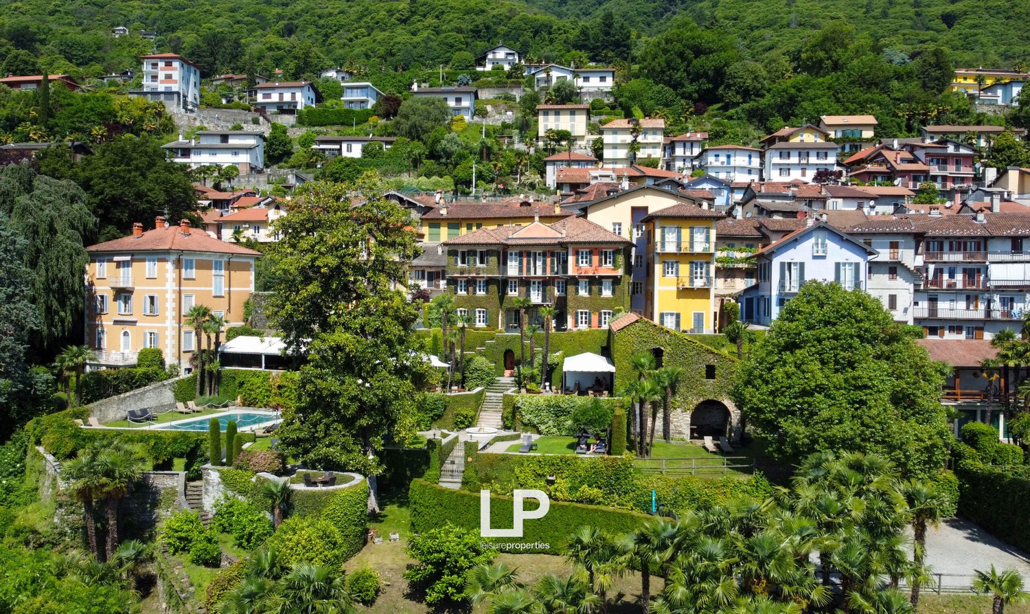 Cluster of houses in a hillside community, multiple pools, lush greenery, trees, distant mountain range