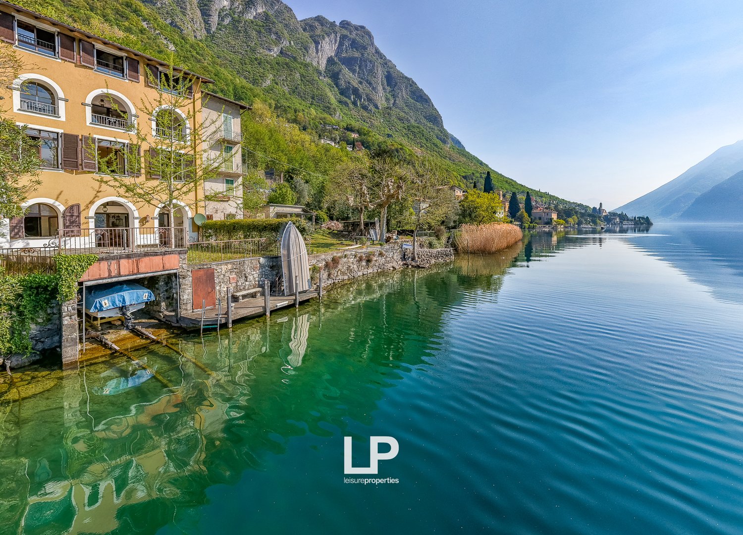House on the lake, with a dock, surrounded by mountains and greenery