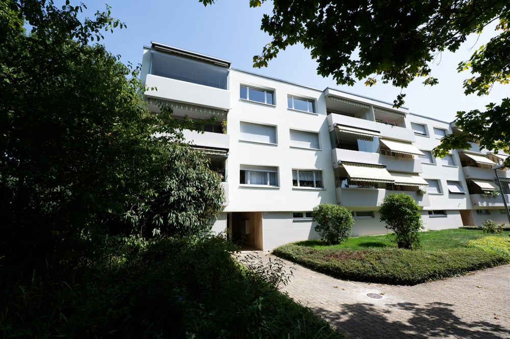 5 story building, white exterior, multiple balconies, brick driveway