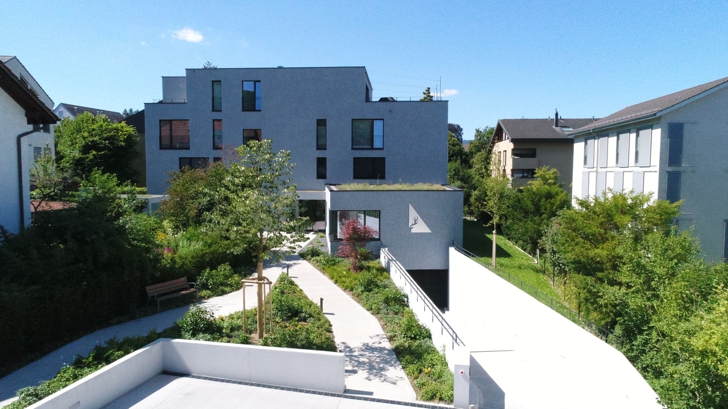 Modern architecture, large grey walls, multiple windows, concrete driveway, garden with pathway