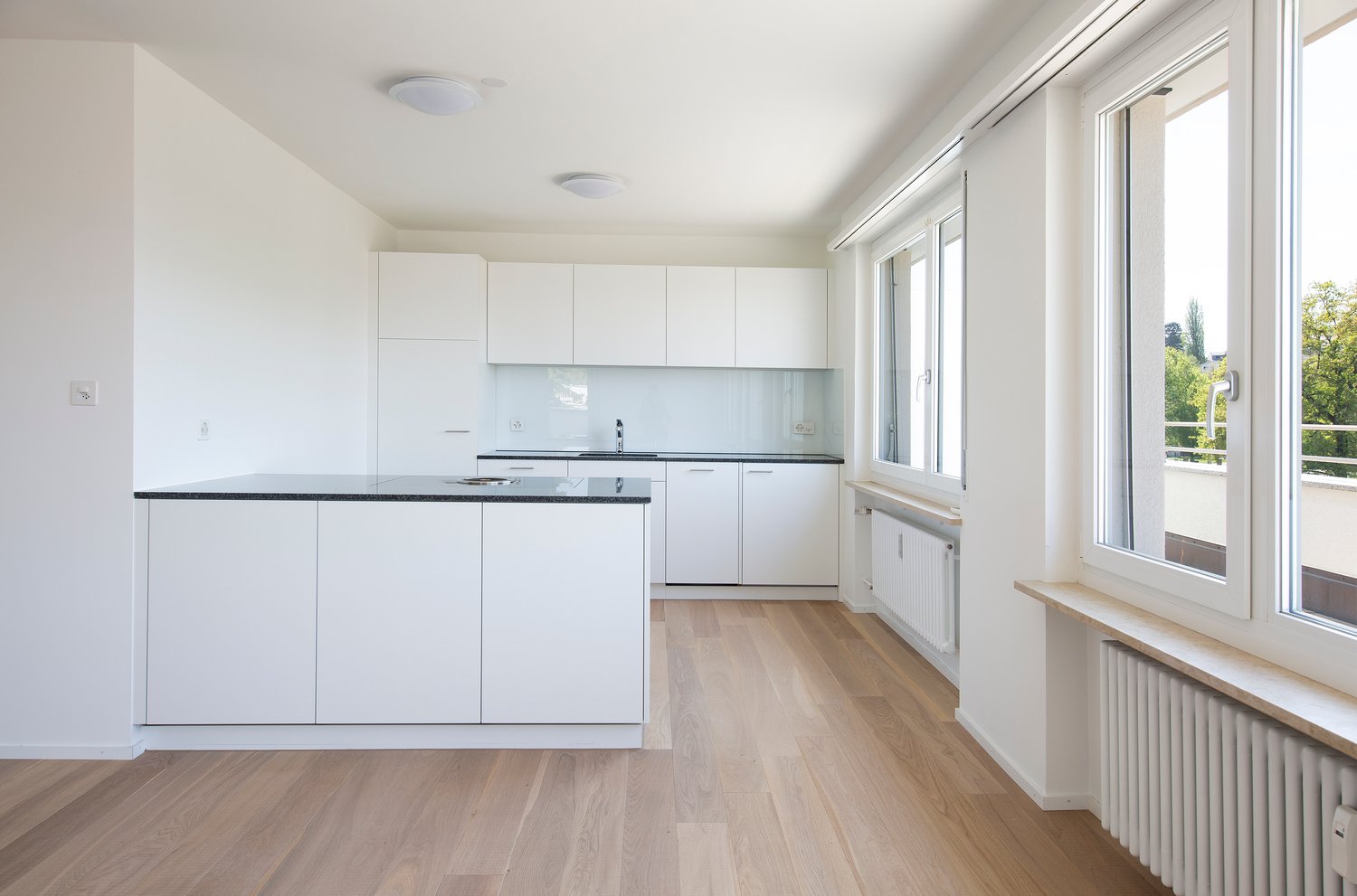 modern kitchen with white cabinets, black countertops, stainless steel faucet, and ample windows
