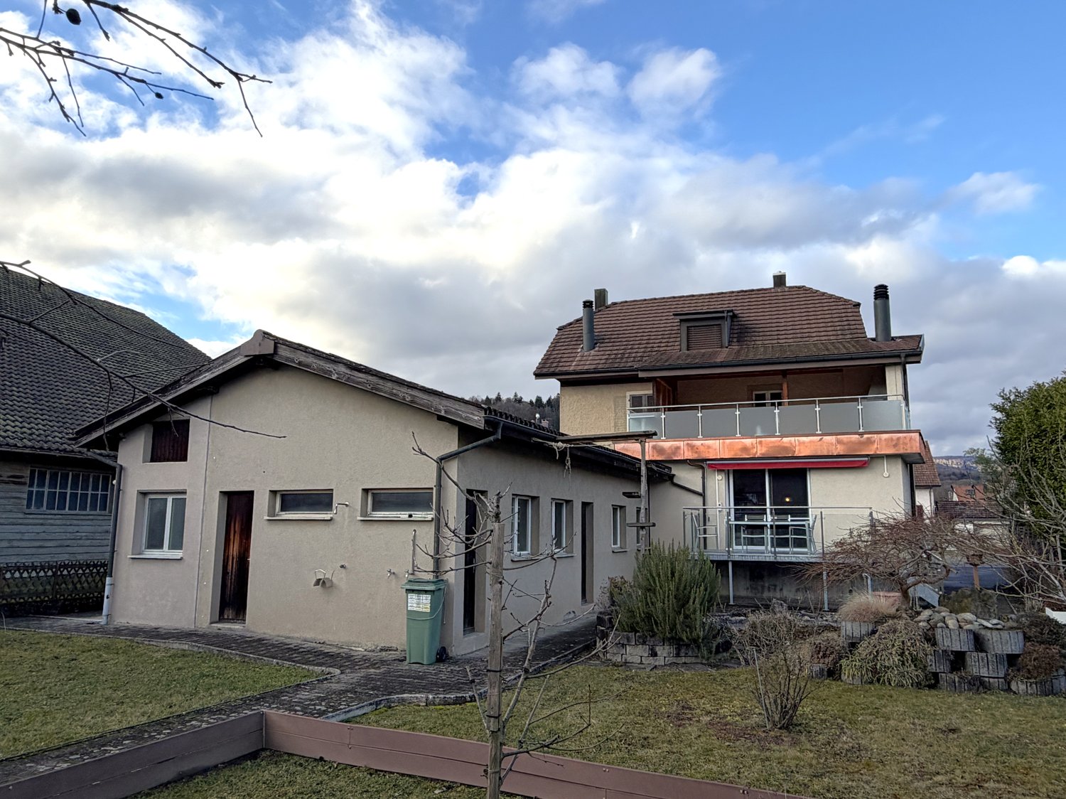 2 story house, brown roof, balcony, green trash bin, garden, fence