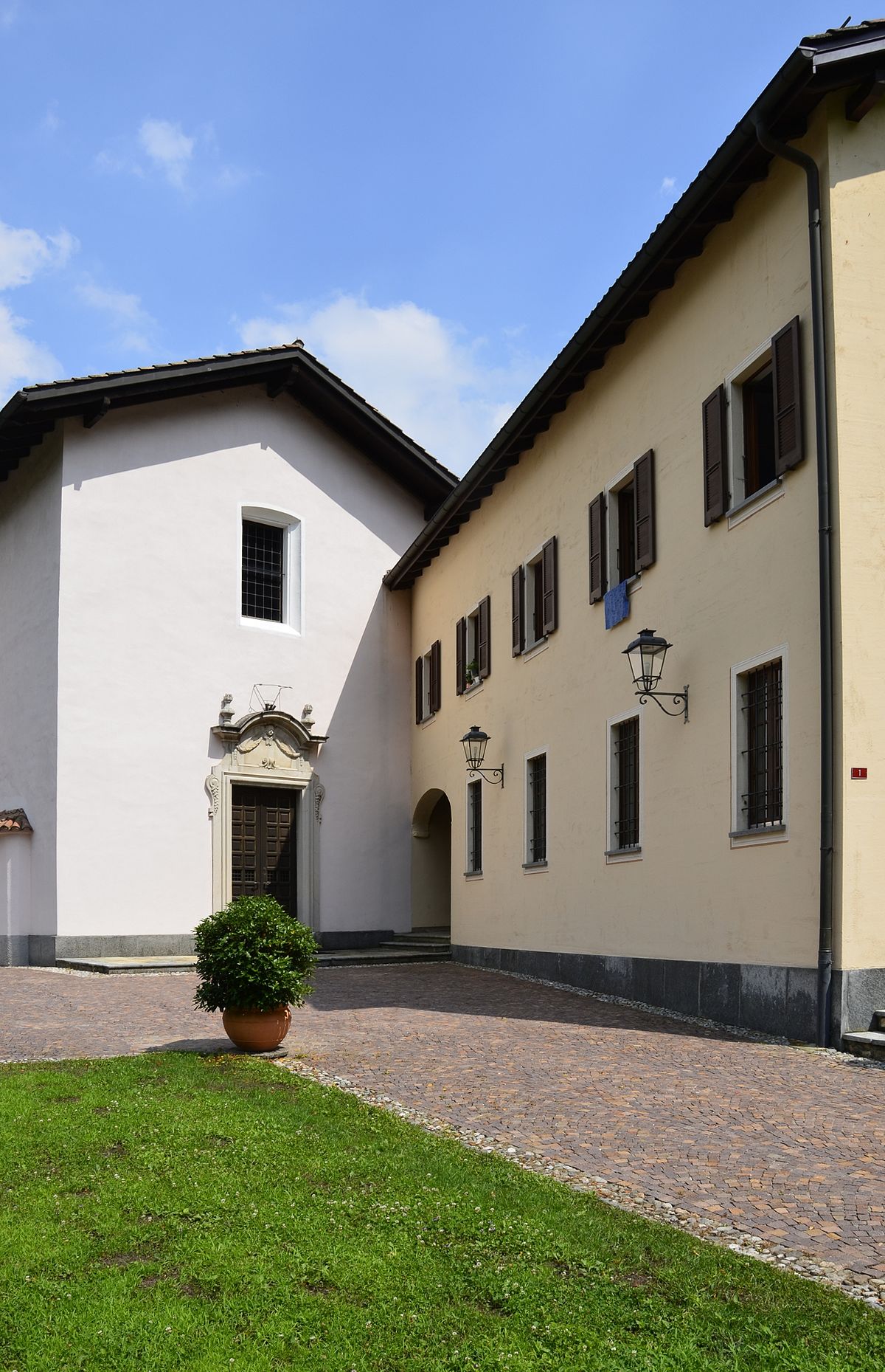 Two story building, brick roof, two entrances, brown wooden door, stone wall, large windows, brown grass, potted plant