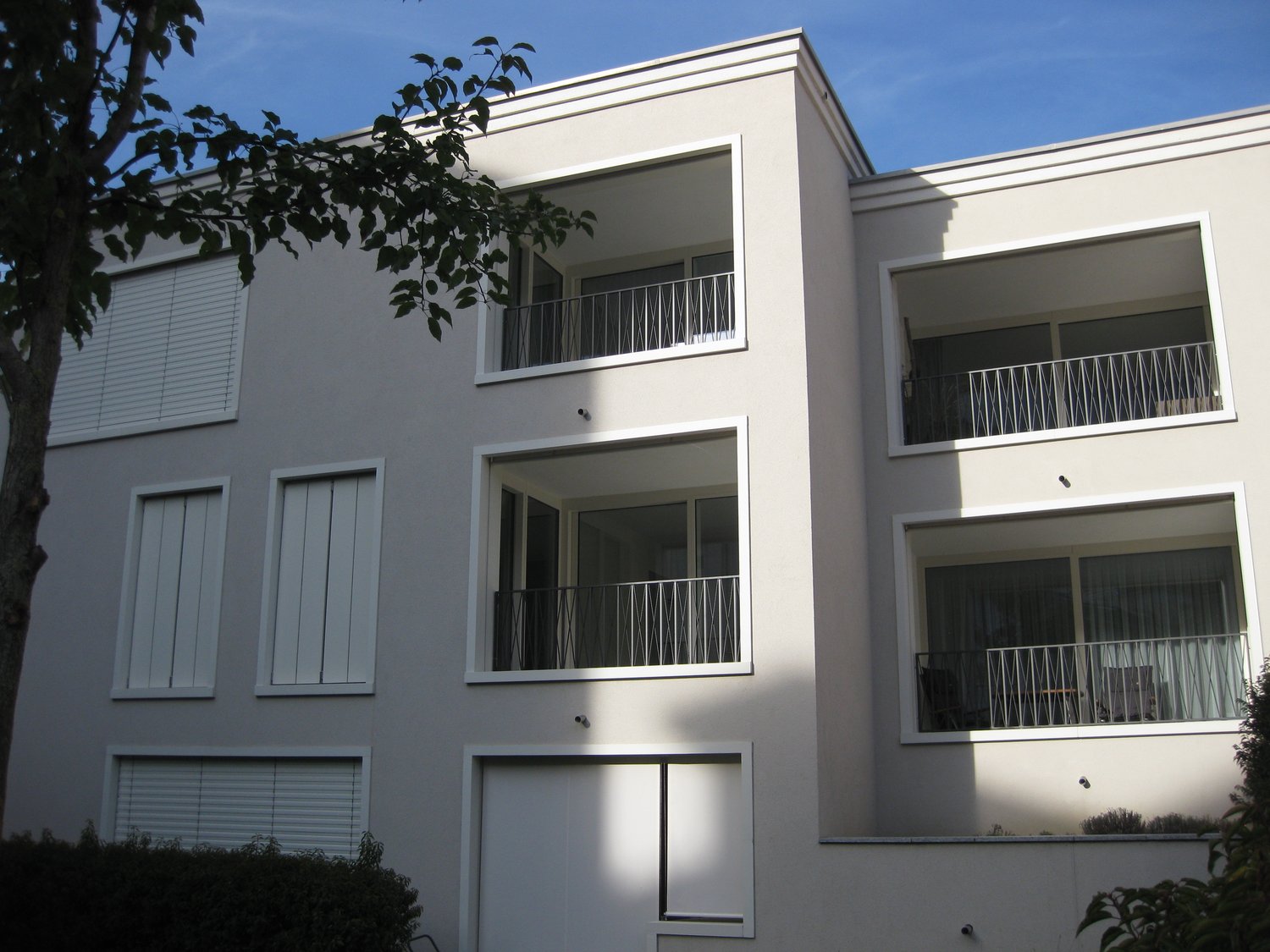 3-story modern building, white exterior, multiple balconies, security cameras
