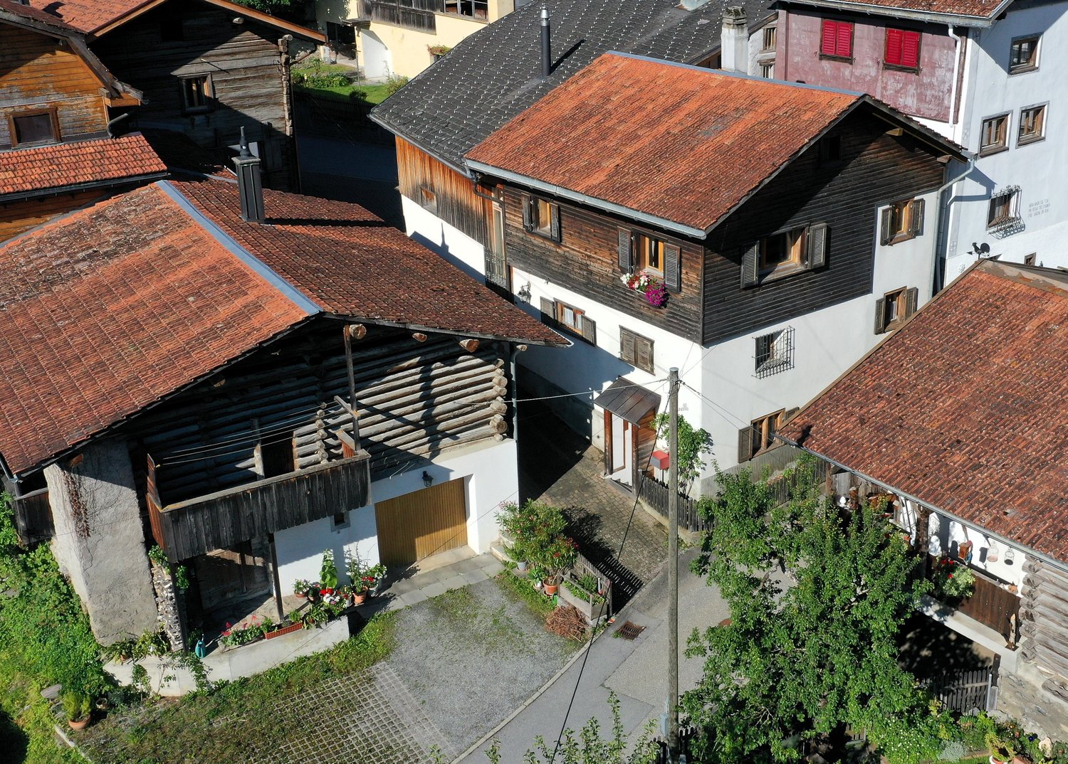 group of wooden houses with tiled roofs, one with wooden balconies, plants, and shrubs