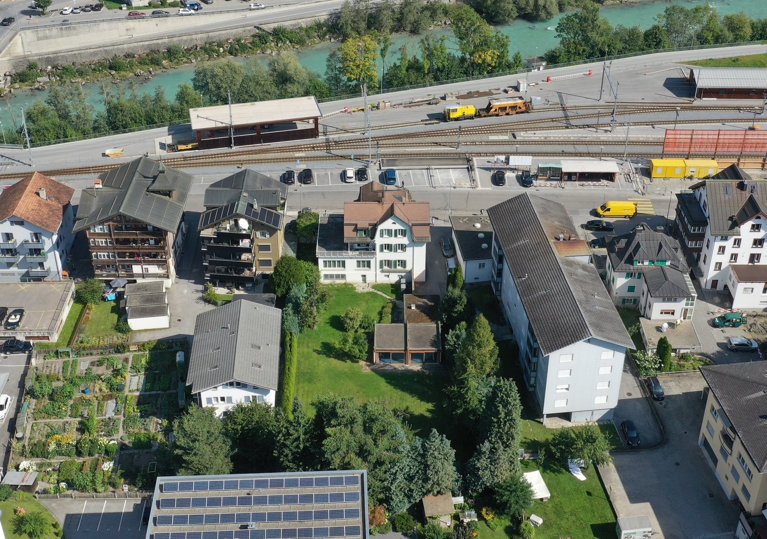 Large building complex, multiple buildings, several parking spaces, garden area with vegetables, trees and solar panels