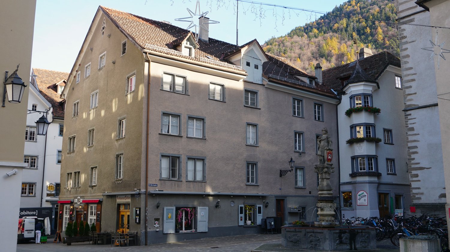 3 story building, multiple windows, red roof, statue in front, bicycles parked