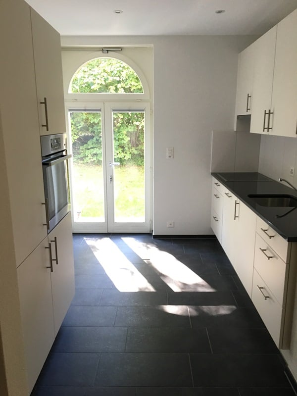 modern kitchen, large windows, tiled floor, white cabinets, stainless steel sink, built-in oven
