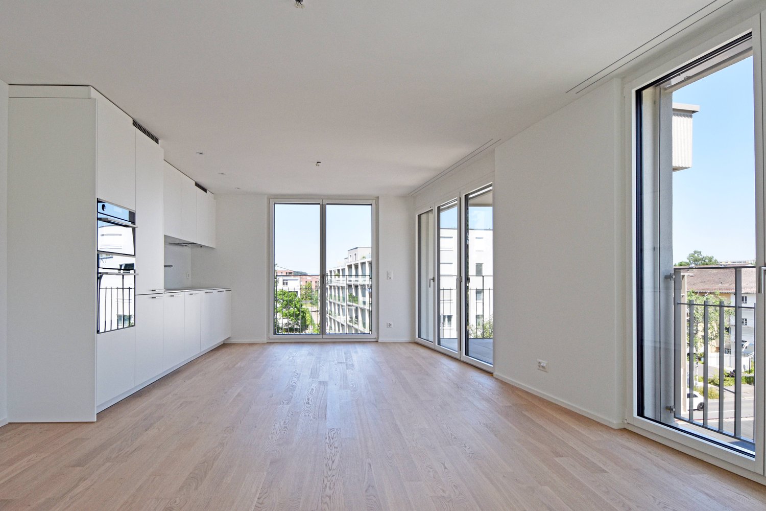 Empty living room with wooden floor and large glass doors to the balcony.