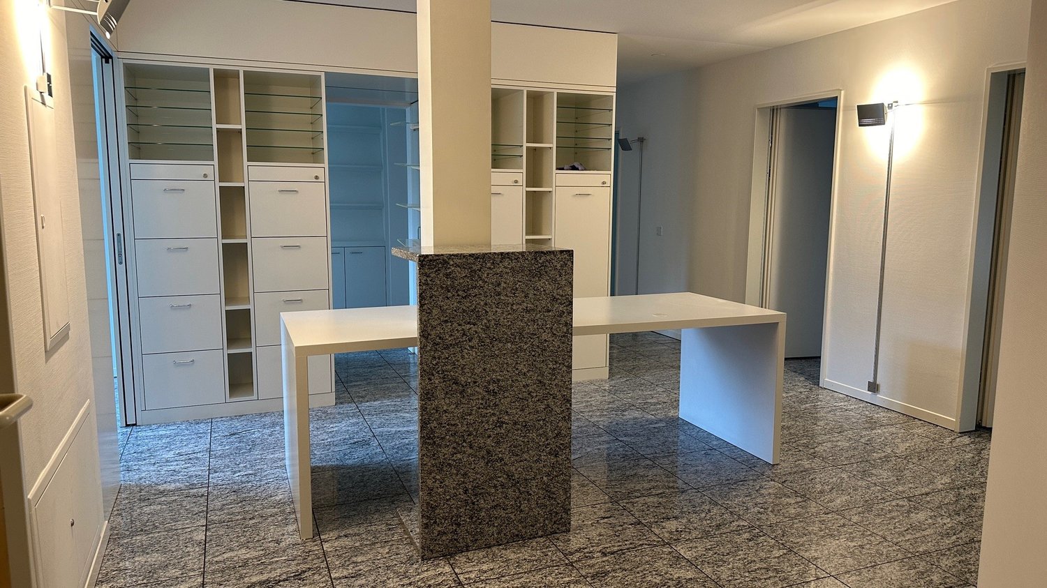 Spacious bedroom with built-in closets, a granite-topped island, and a dining table. The room has a modern, minimalist design with neutral colors and tile flooring.