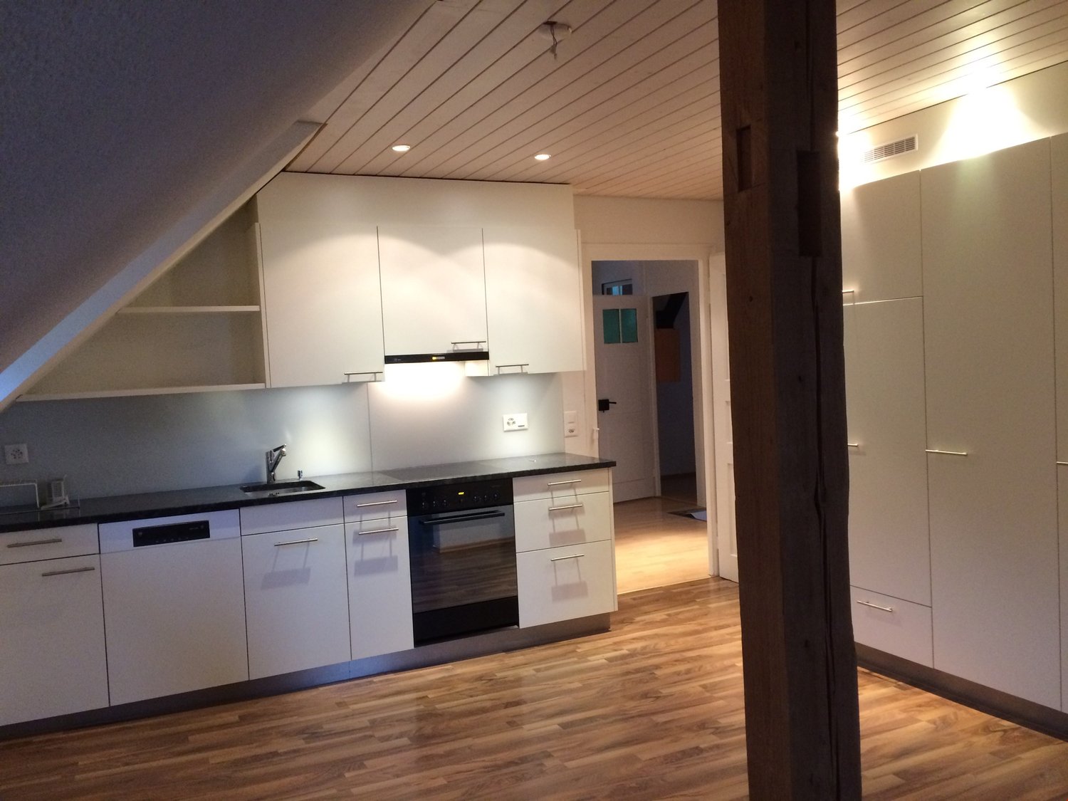 Modern kitchen with white cabinets, black countertops, dishwasher, washing machine, sink, faucet, oven, wooden floor