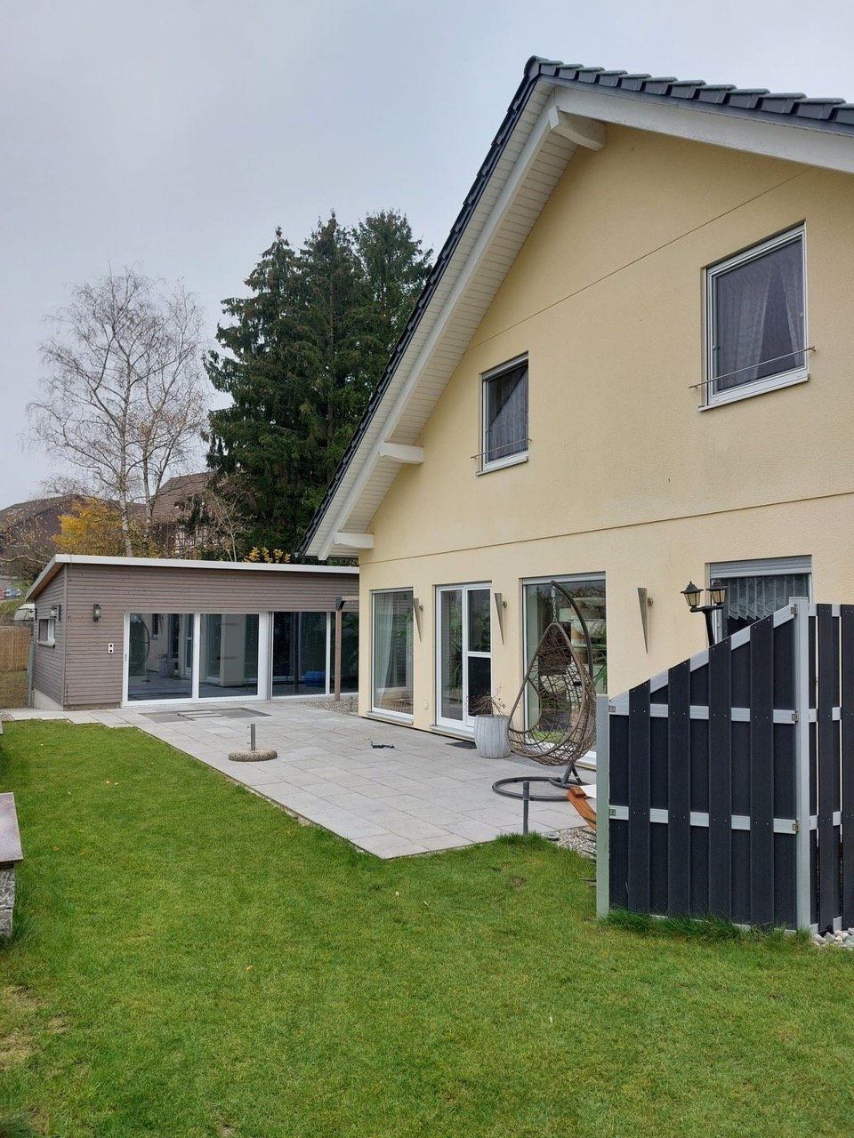 detached house with terrace, large garden, patio, lounge chair, lamp, paved terrace, fence, sliding doors, windows, outdoor seating area, potted plant, exterior wall