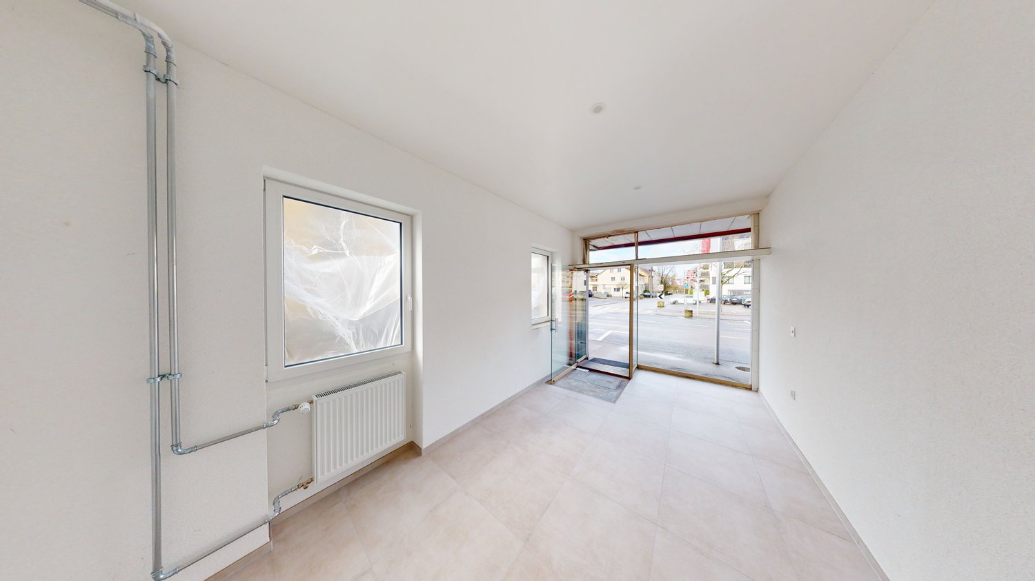 Large room, white walls, tile floor, glass window, radiator, two doors, leading to a parking area