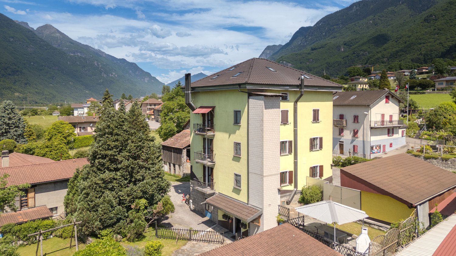 Mountain view residential area with several houses, brown roofs, yellow walls, small gardens, and nearby mountains