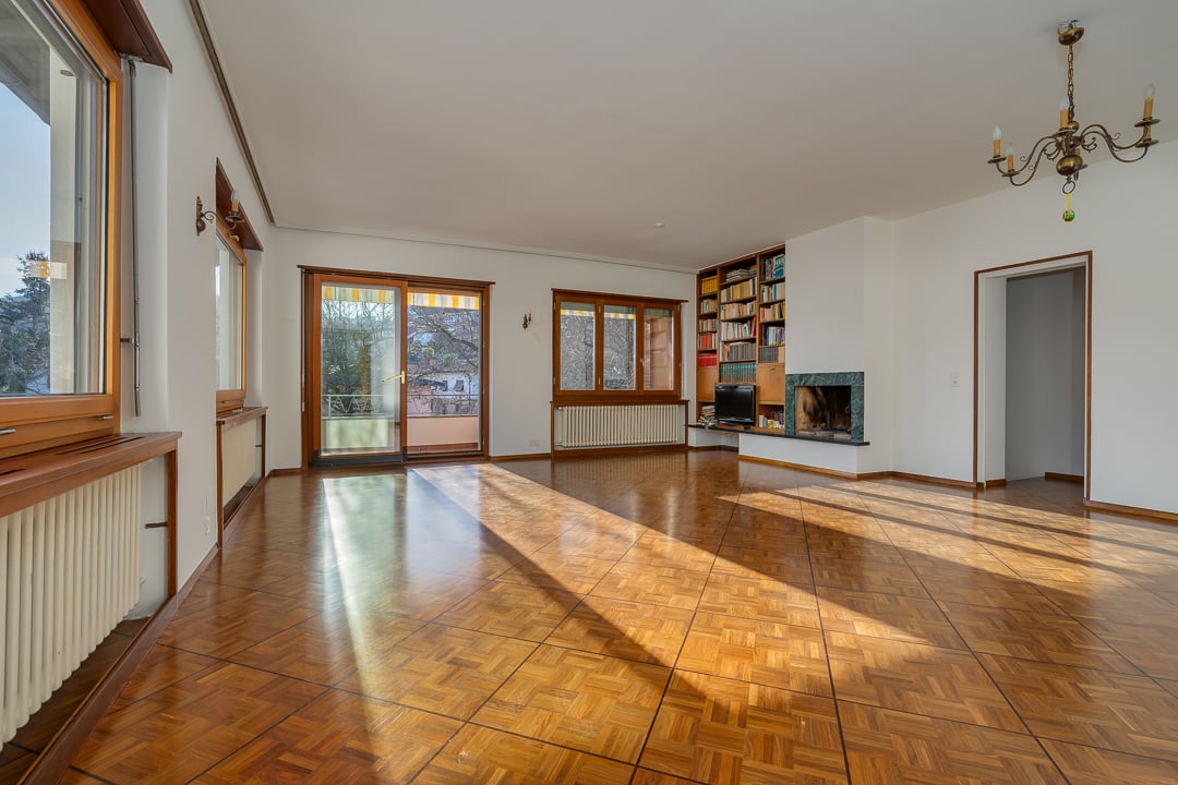 Spacious living room with hardwood parquet flooring, large windows, a fireplace, and built-in bookshelves.
