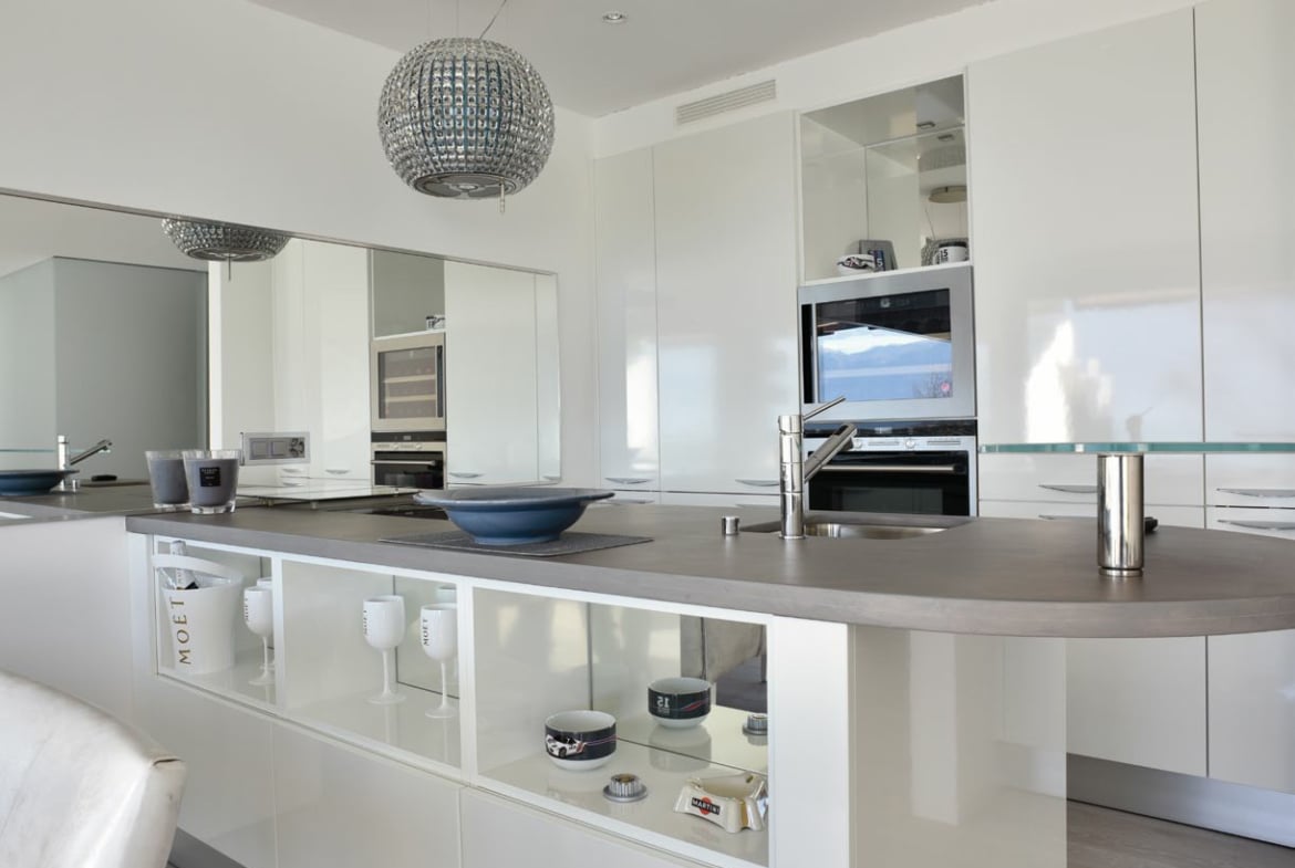 Modern kitchen with stainless steel appliances, granite countertops, white cabinetry, center island, pendant lighting, mirror wall