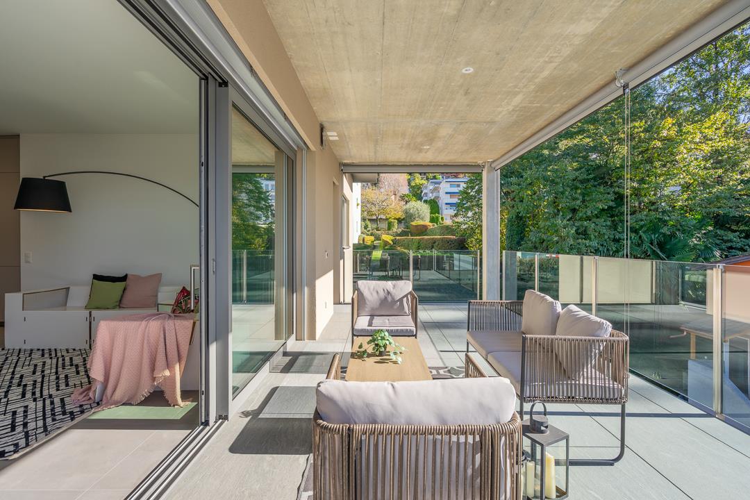 modern styled living area with beige furniture, glass walls with balcony, trees view, dark tiled floor