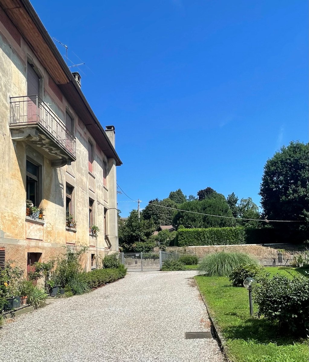 Old building with balcony, gravel driveway, garden, green grass, plants, trees