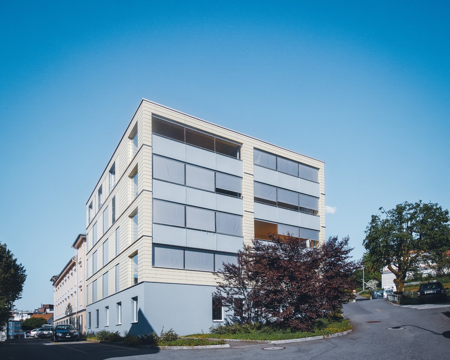 modern design, several floors, glass windows, beige and white exterior, parking area in front