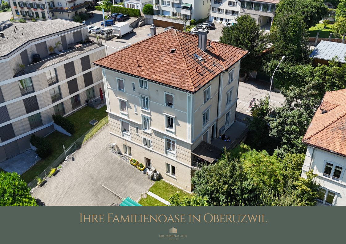 An apartment building with a red roof, multiple windows, and surrounded by greenery. Parking area in front with a white van parked.