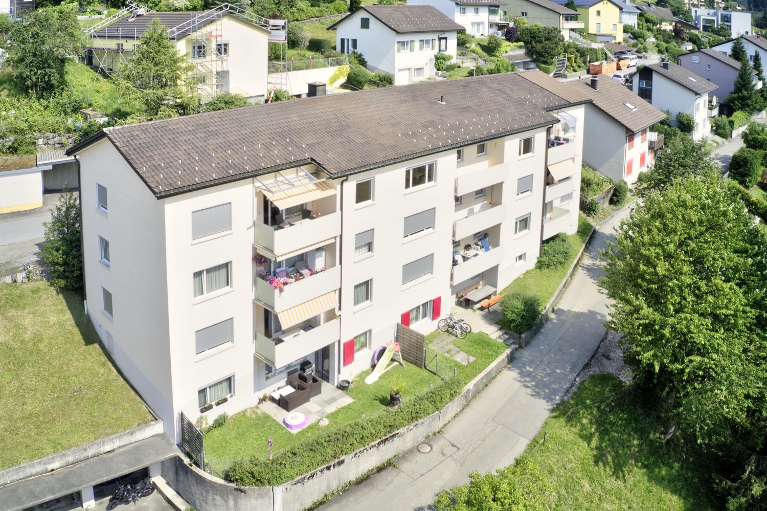 A multistory apartment building with several balconies, surrounded by greenery and a pathway.