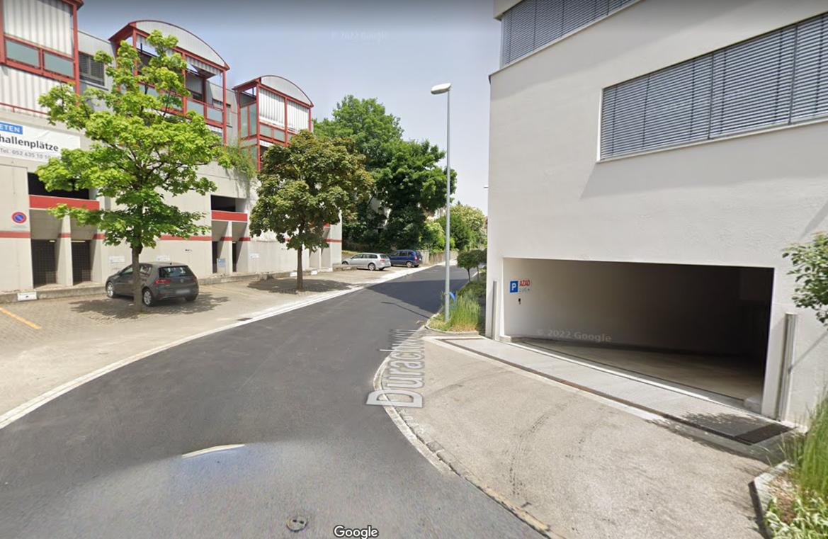 Building facade, visible parking area, garage entrance, streetlight, cars parked on the side.