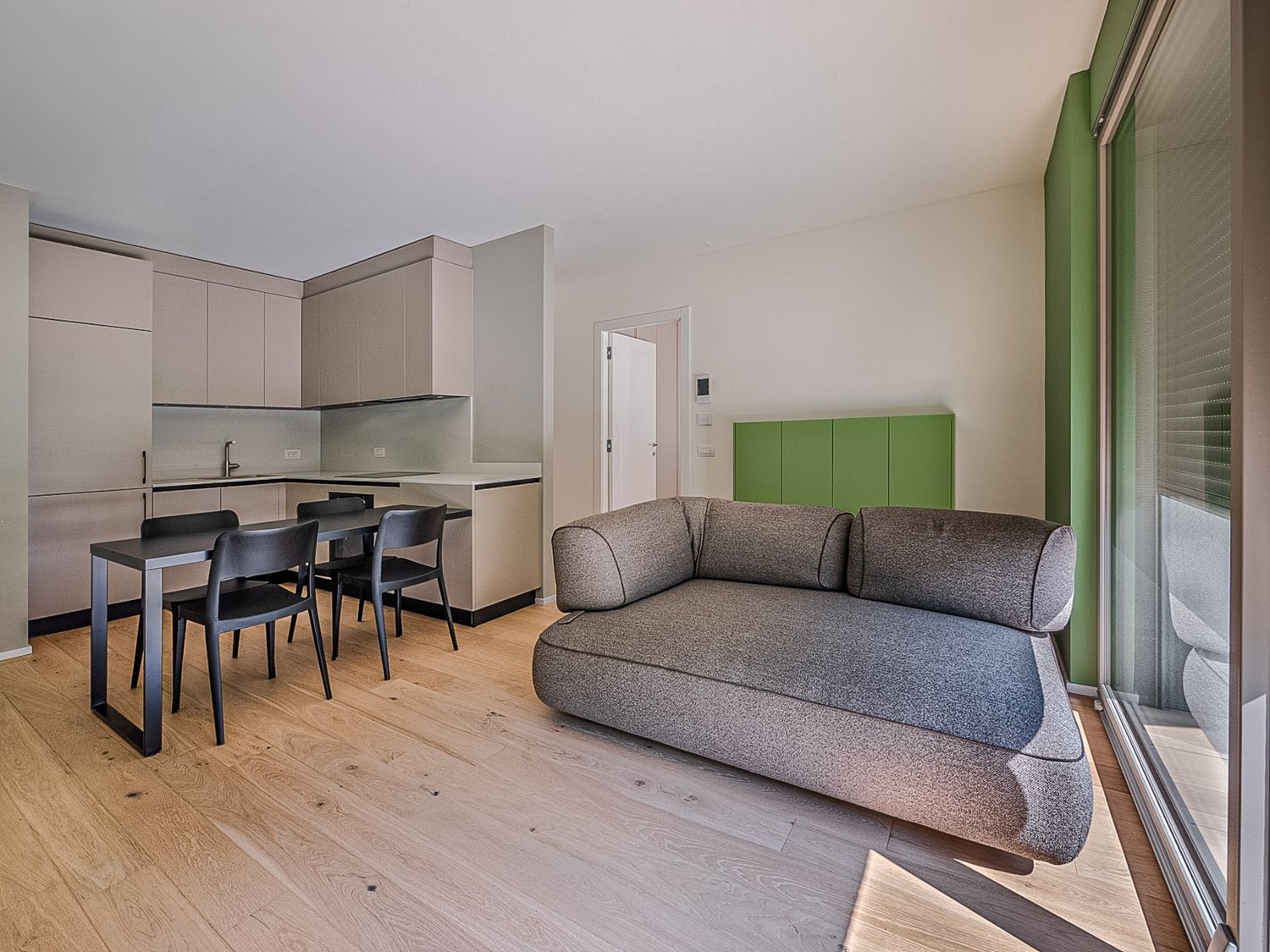 Open space, grey couch, glass wall, light wood floor, black dining table with chairs