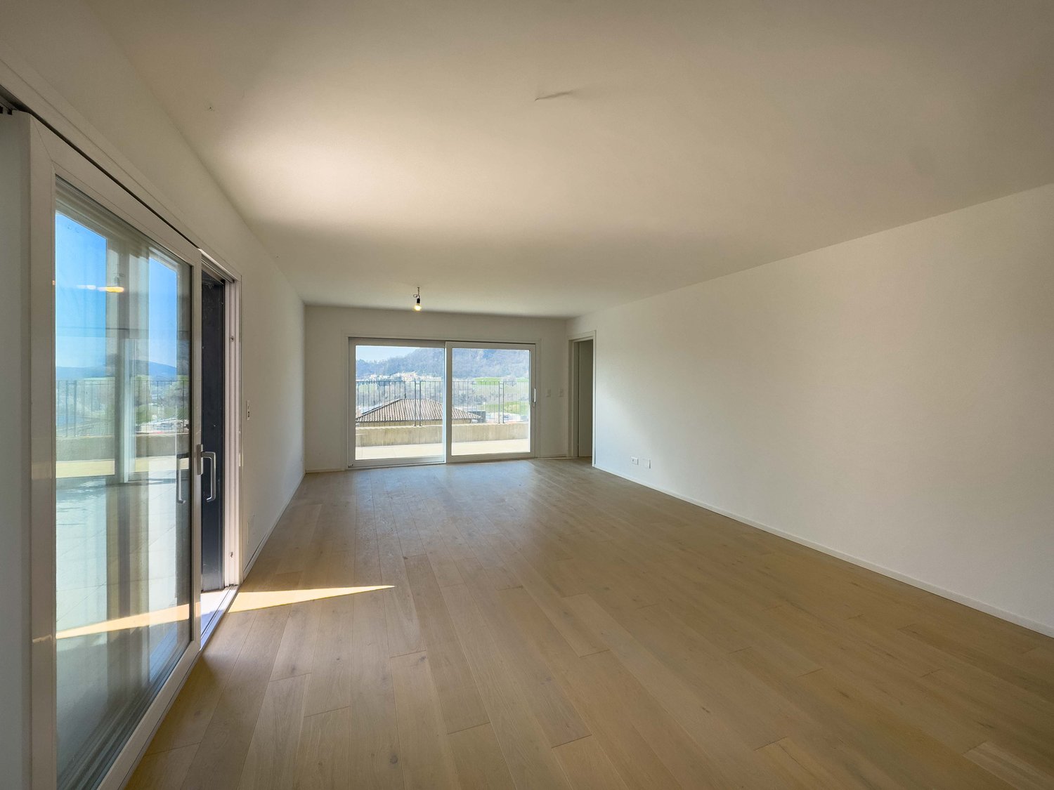 Empty room with glass sliding doors leading to balcony and sliding glass doors with view of mountains.