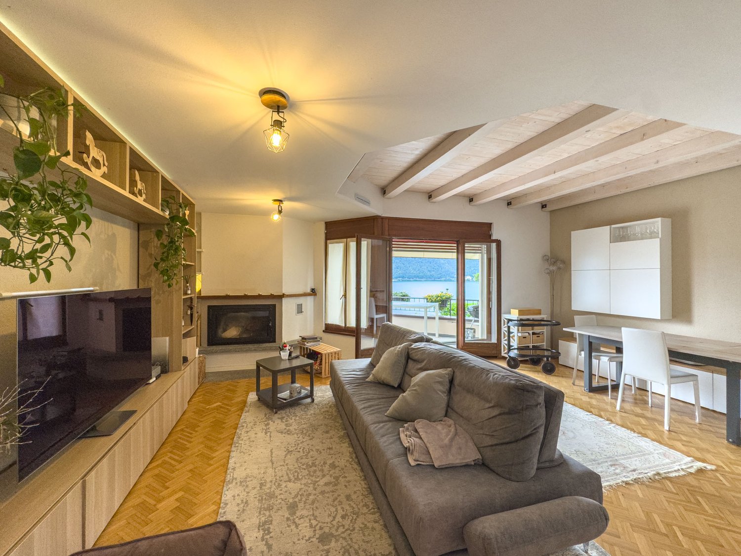 living room with gray couch, table, TV, fireplace, dining table, wooden floor, balcony with sea view