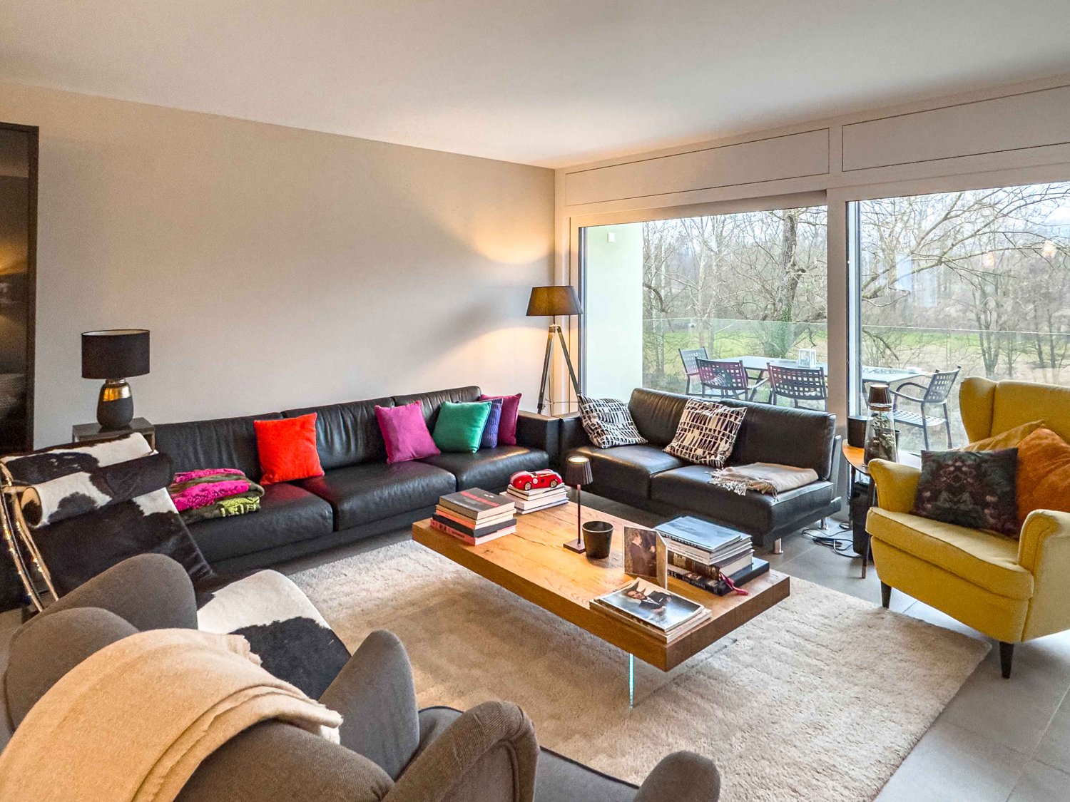 Modern living room with glass doors leading to a balcony overlooking the landscape, full leather couches, large windows