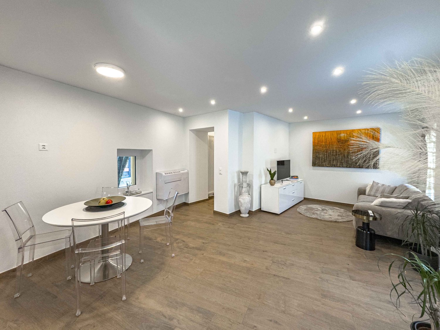 round table, glass chairs, flat screen TV, small white cabinet, grey sofa, rug