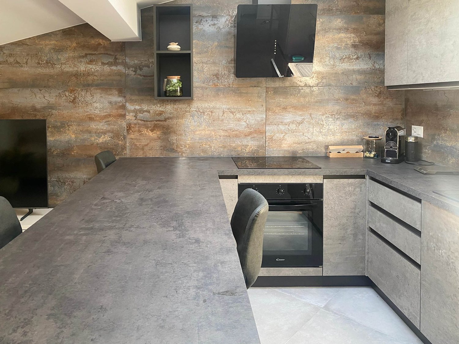 modern kitchen, long counter, gray wall, black appliances, two shelves, large cabinet, gray flooring