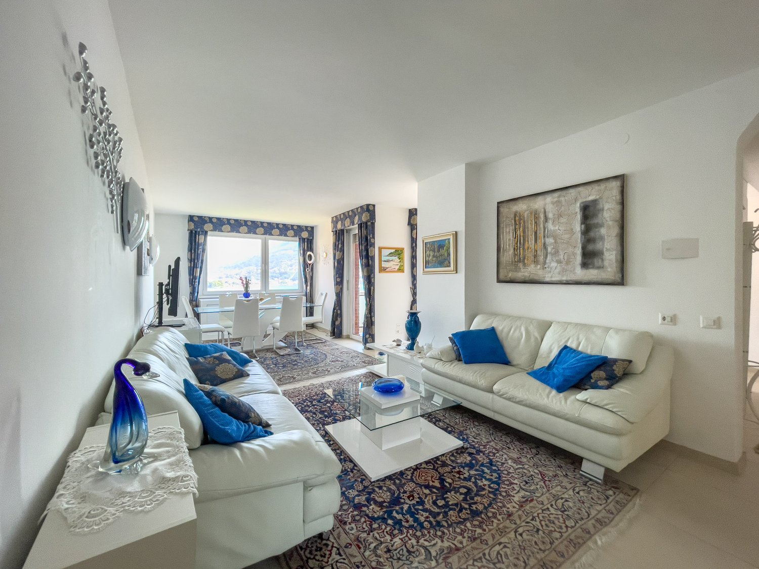 two sofas, glass center table, large area rug, wall paintings, window with curtains, balcony