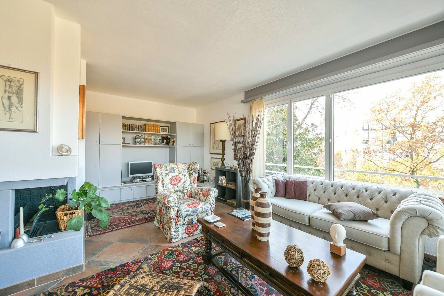living room with fireplace, couch, chair, coffee table, television, bookshelf, picture frames, vases, candle, rug