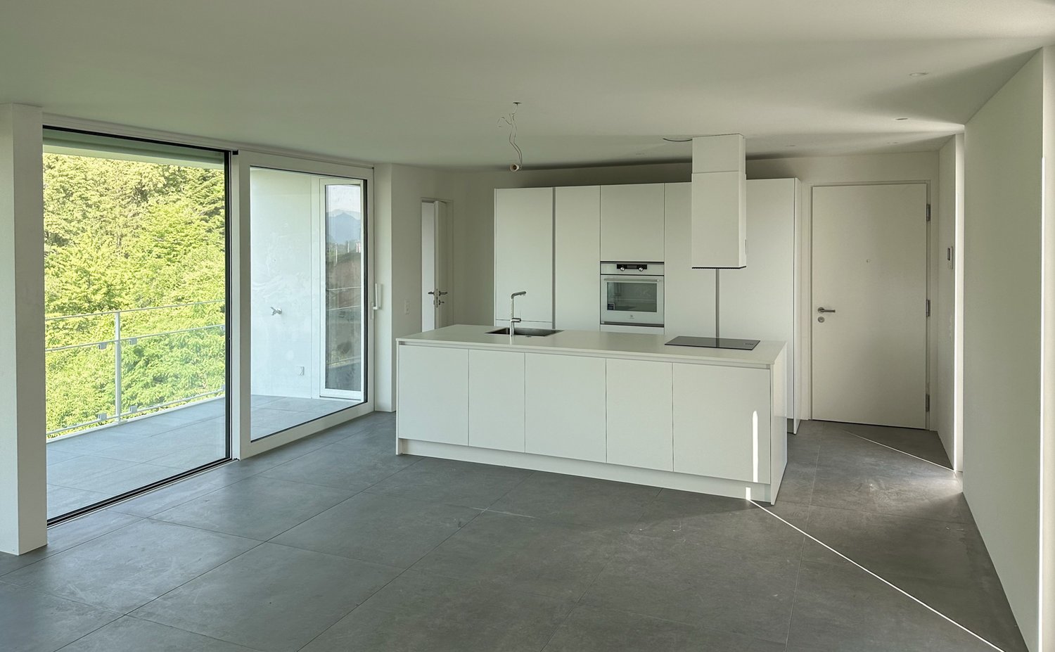 Sliding glass doors to a balcony, modern white kitchen with a black countertop, oven and sink
