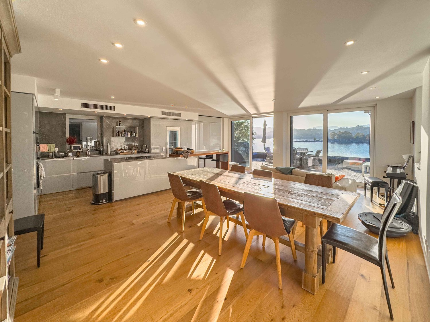 wooden dining table with 6 chairs, glass wall with lake view, kitchen, couch, bookshelf