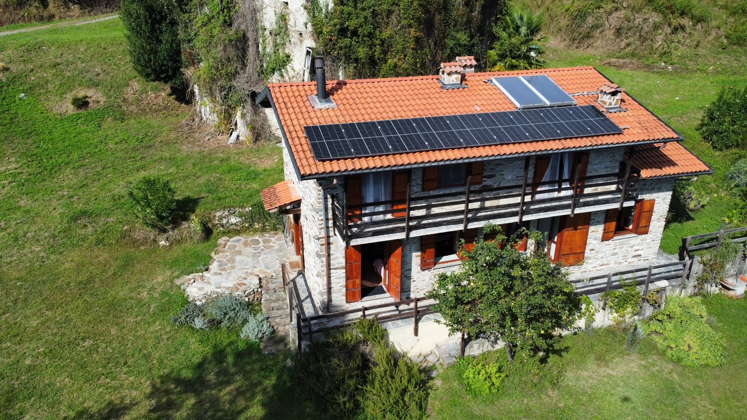2 story house, stone walls, red roof, raised ground floor, solar panels, terrace