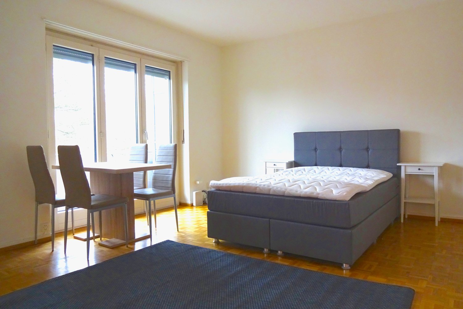 bedroom with a bed, table, chairs, windows, hardwood floor