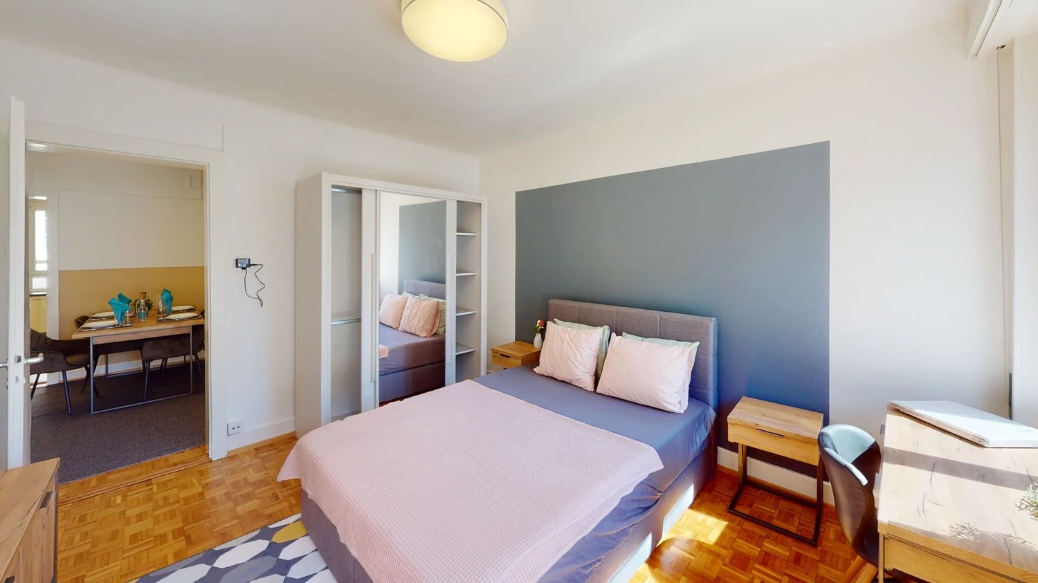 Bed with pink bedding, wooden nightstand with flower vase, wooden desk, chair, wardrobe, carpet