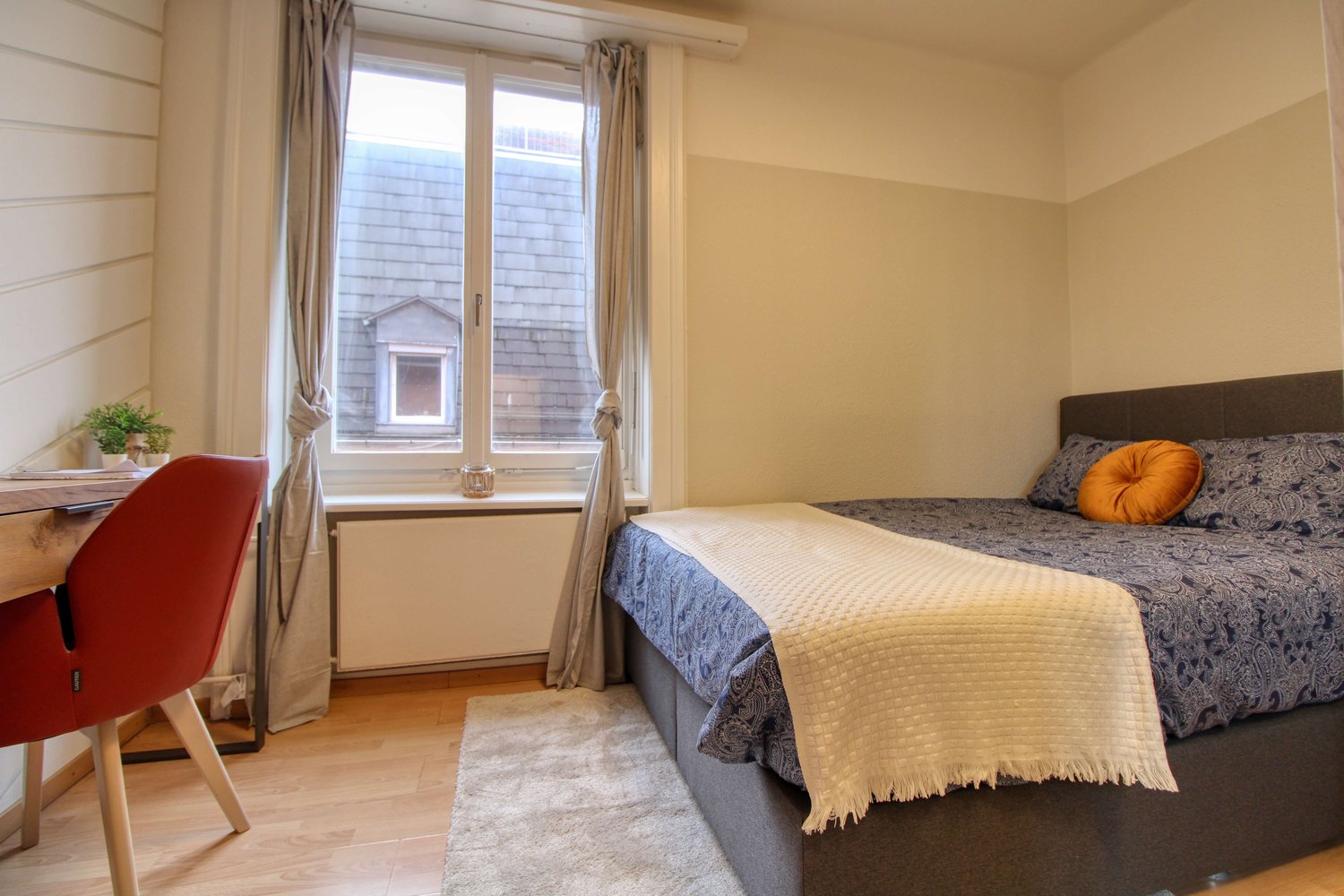 white walls, carpet, desk with chair, bed with pillows, rug, window with curtain