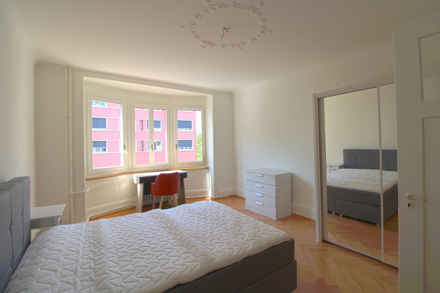 modern bedroom, white walls, gray bed, white bed sheet, desk with orange chair, arched window, white dresser, glass door leading to another bedroom