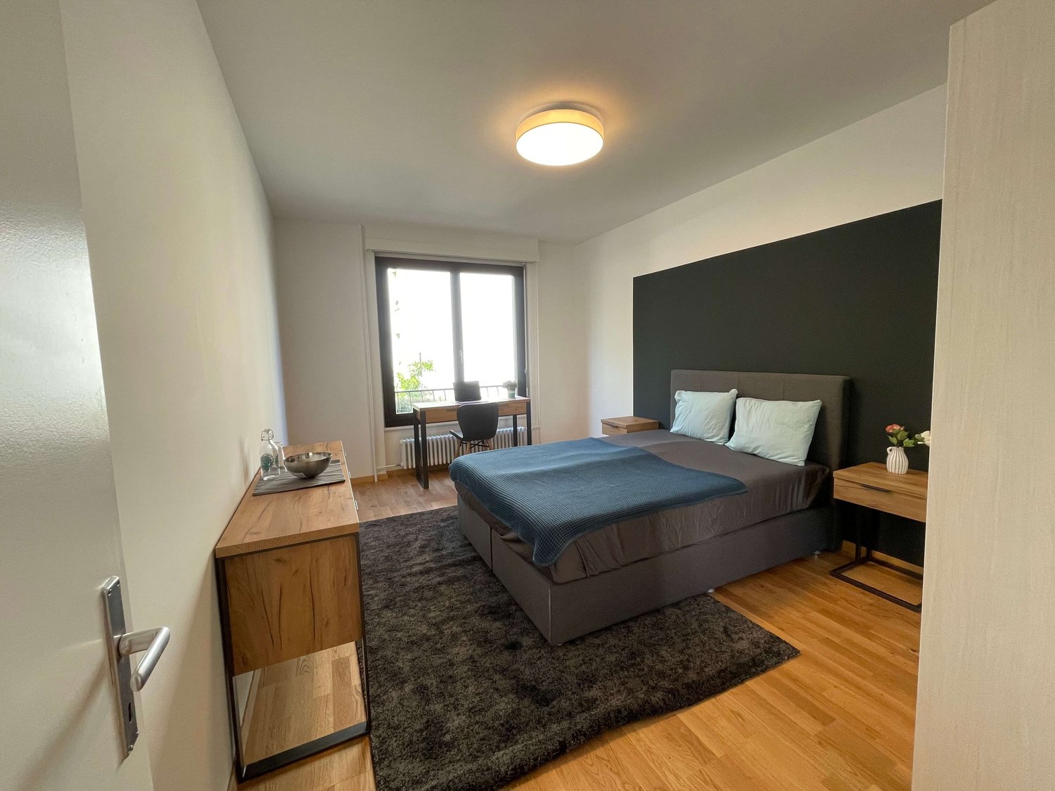 bedroom with bed, desk, chair, radiator, window, rug, lamp, nightstands, flowers