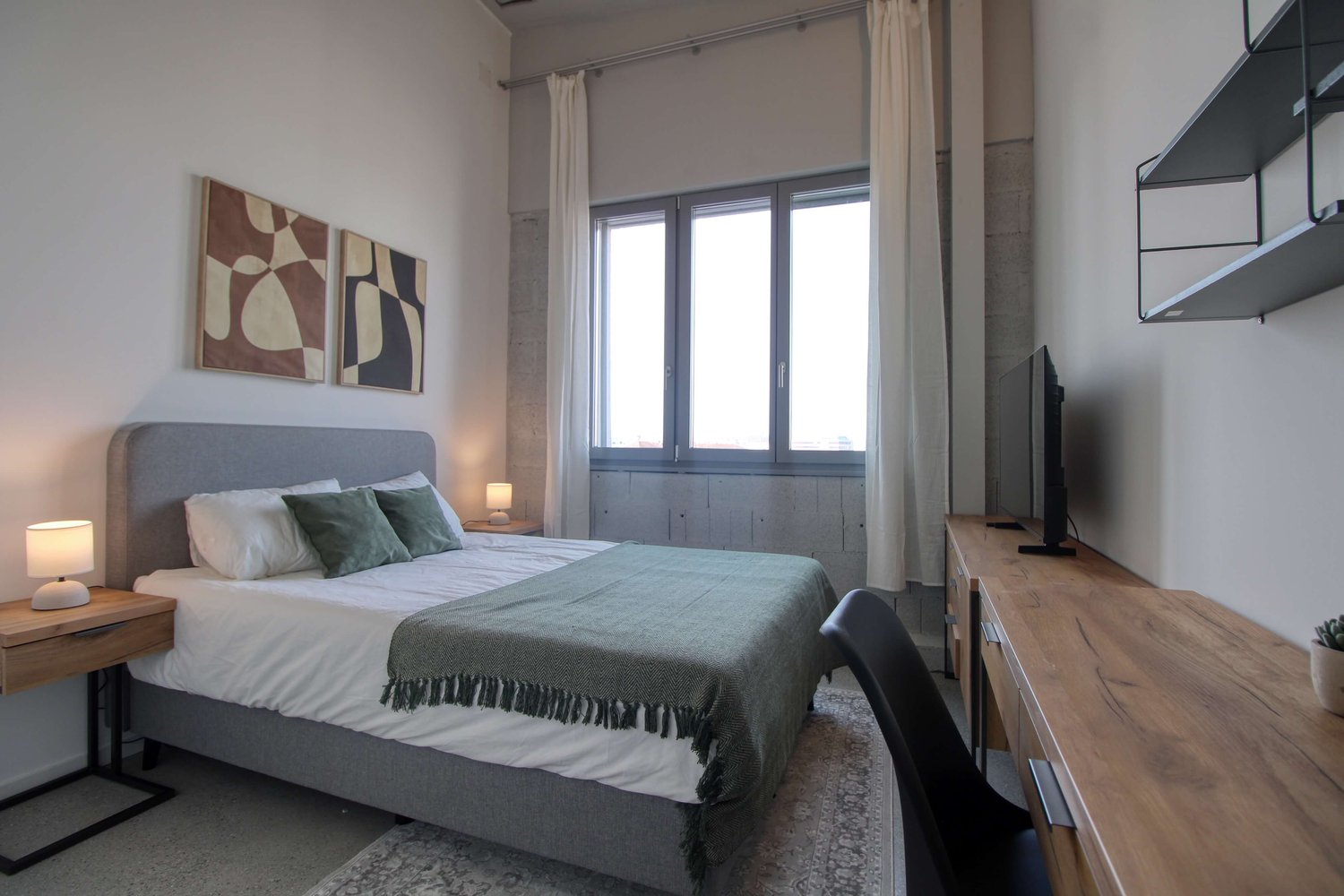 Bedroom with bed, nightstands, desk, chair, TV, artwork, and rug