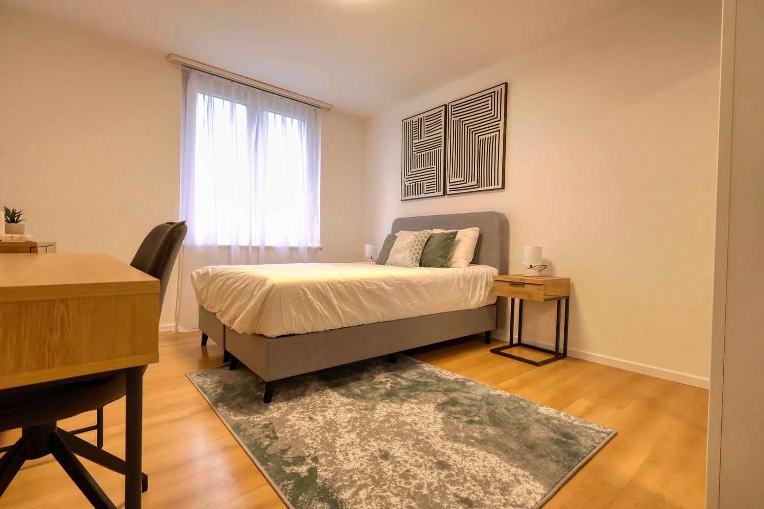 Bedroom with bed, desk, chair, rug, nightstands, lamps, and window with curtains