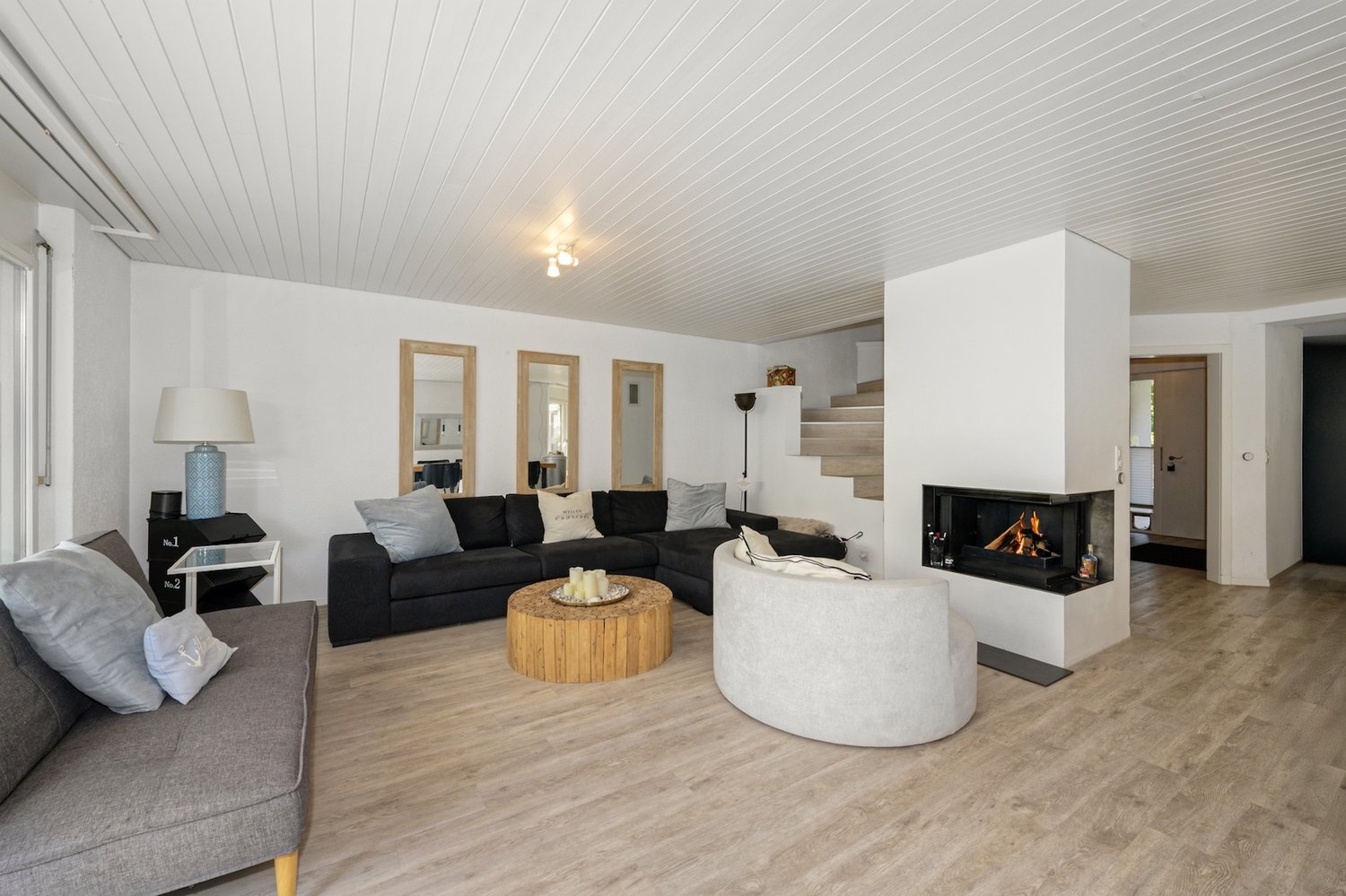 Living room with wood flooring, fireplace, black sofa, white walls, wooden coffee table, two side tables, lamps